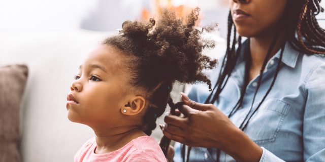 Little girl getting her hair twisted by her mom.
