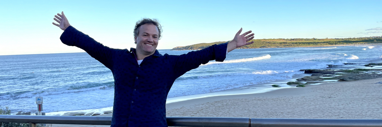 Contributor standing in front of the ocean with a big grin and arms open wide