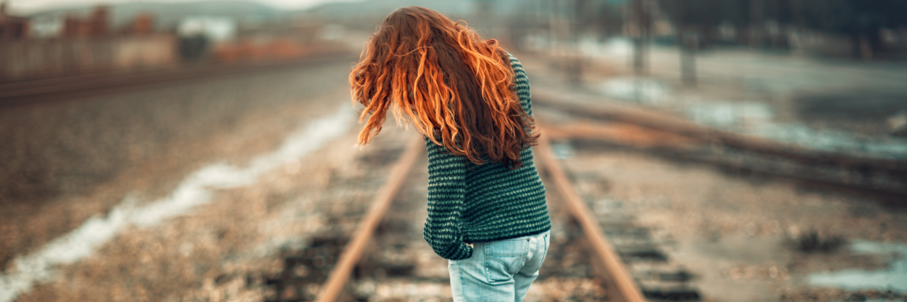 A woman with long red hair walking on a train track
