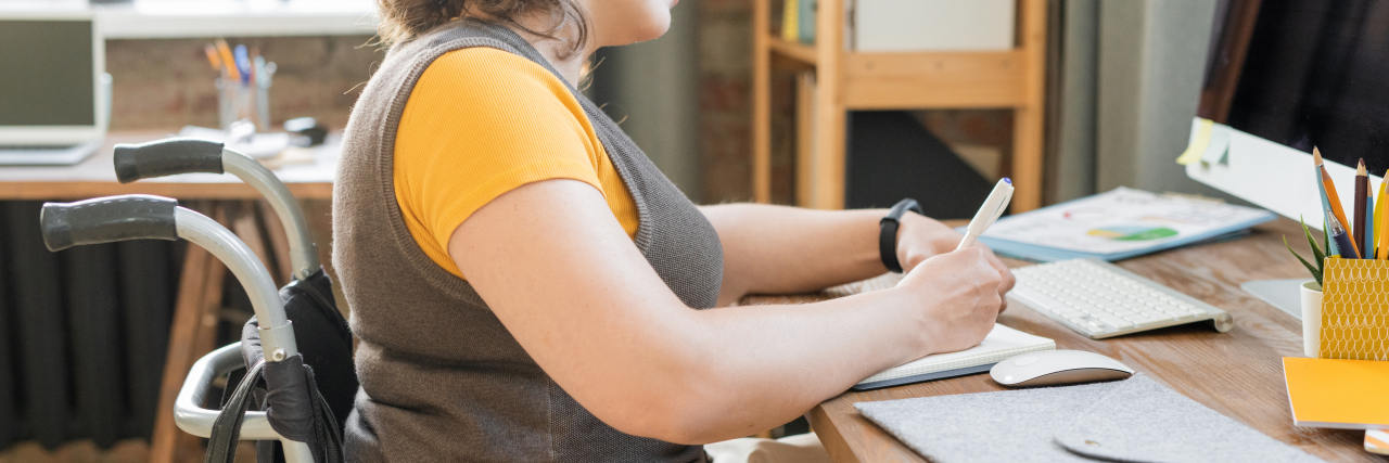 Helpful Ways to Cope in Life With a Disability Close-up photo of a woman wearing a gray vest, an orange shirt, and khaki pants writing while she sits in a wheelchair.