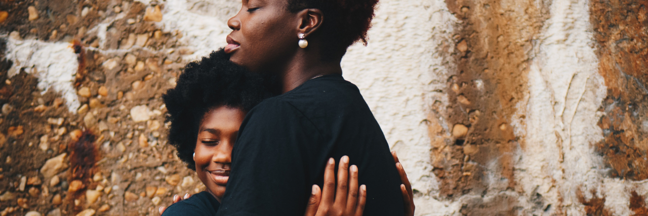 photo of two Black women embracing in front of a wall