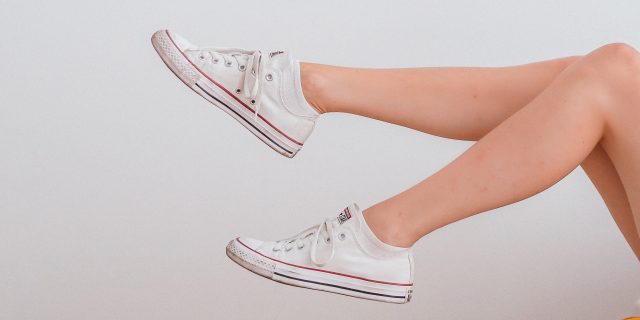 photo of a person's legs in white sneakers against a white wall