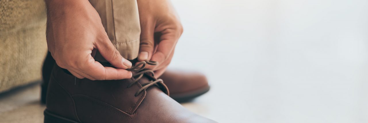 Challenging Everything as a Mindset in Life With Cerebral Palsy A man of color wearing a light blue button-down shirt, khaki pants, and brown shoes reaches down to tie his shoes.