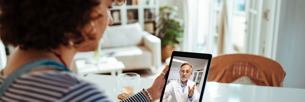 Being Off Medication Isn't Always Good for Mental and Chronic Illness A person with dark curly hair wearing a striped shirt talks to their doctor on a tablet while sitting at a white table.