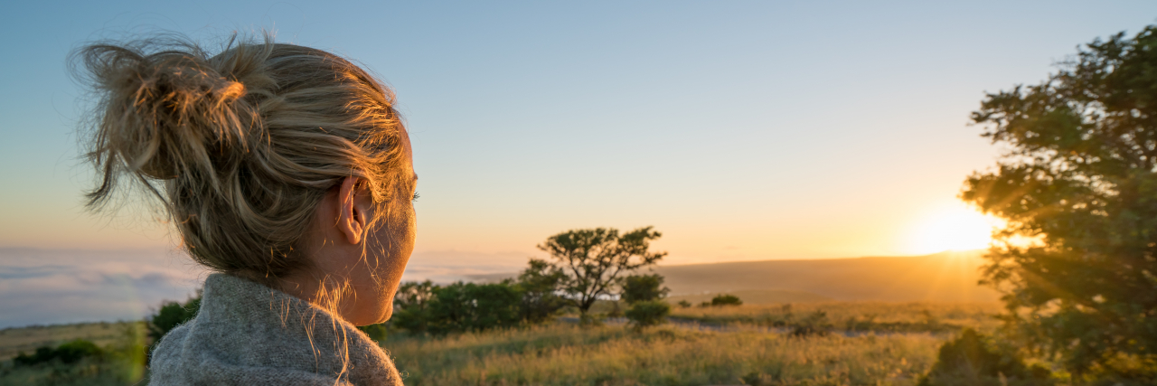 Speaking Out About Neurogenic Bladder to Reduce the Stigma A blonde woman with an updo and wearing a cardigan looks out at the sun.