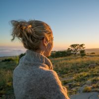 A blonde woman with an updo and wearing a cardigan looks out at the sun.