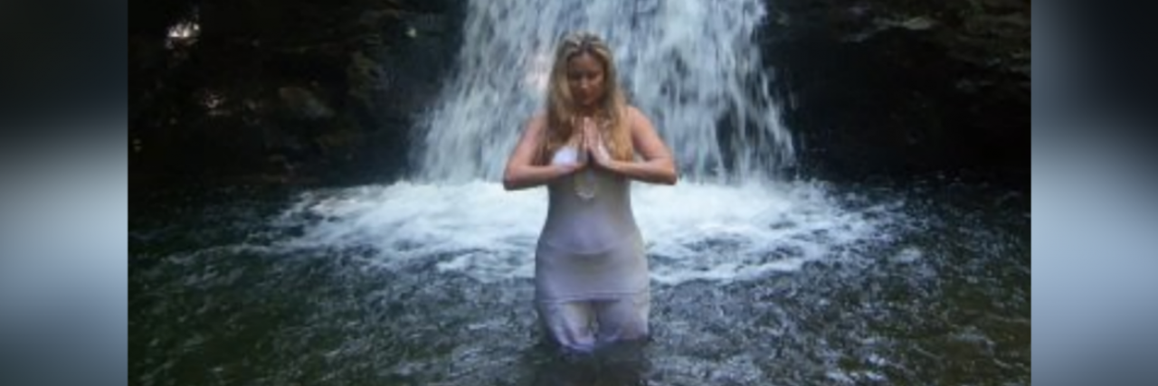 Contributor standing in front of waterfall holding her hands in prayer position