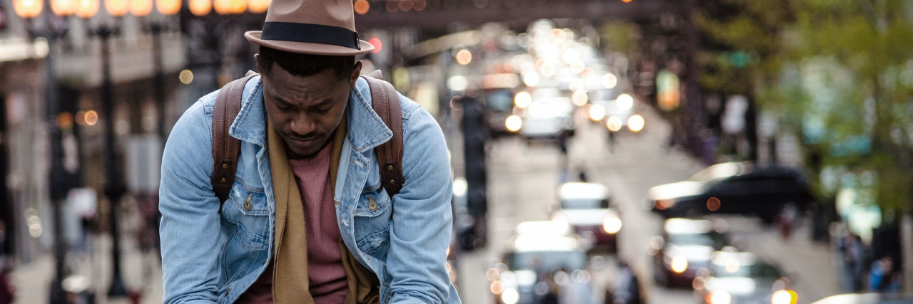 photo of a man sitting on a ledge and looking down with a blurred city behind him