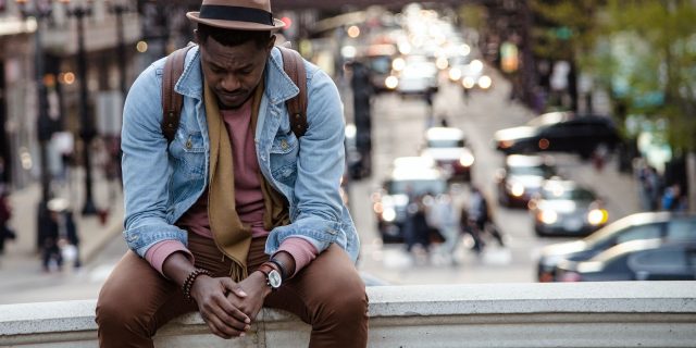 Dr. Ally's Guide to Adverse Childhood Experiences and What We Do About Them photo of a man sitting on a ledge and looking down with a blurred city behind him