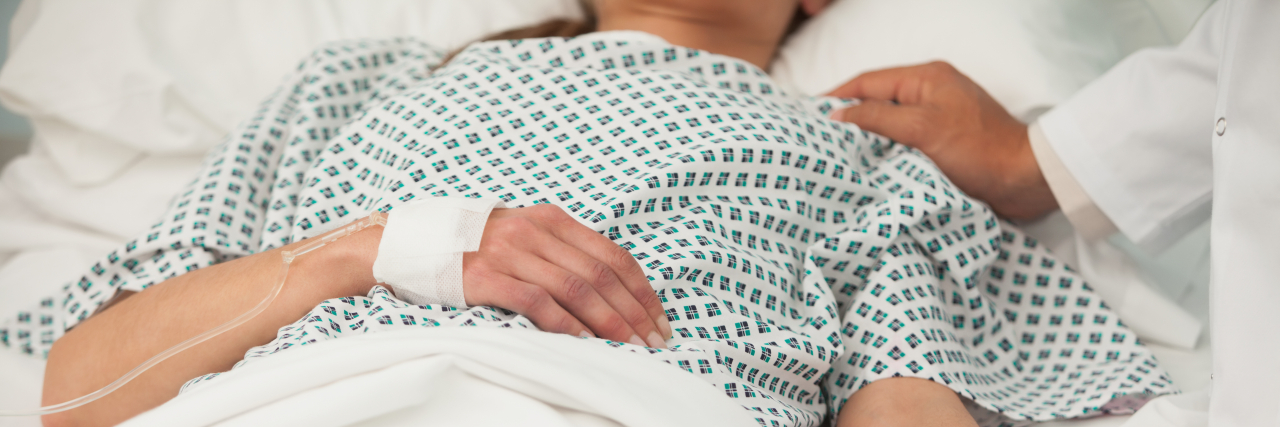 Close-up photo of a woman wearing a hospital gown and lying in a hospital bed.