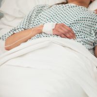 Close-up photo of a woman wearing a hospital gown and lying in a hospital bed.