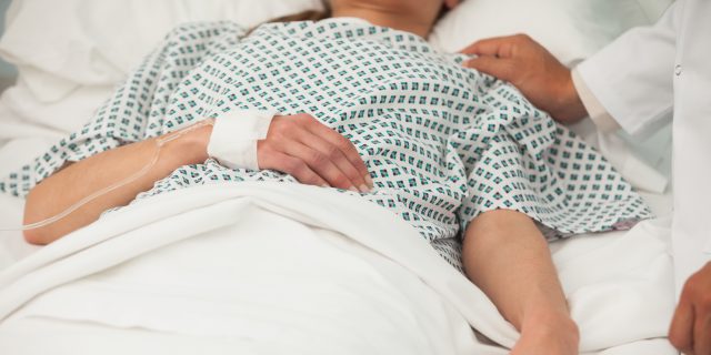 What I Learned When I Faced Medical Trauma From Chronic Illness Multiple Times Close-up photo of a woman wearing a hospital gown and lying in a hospital bed.