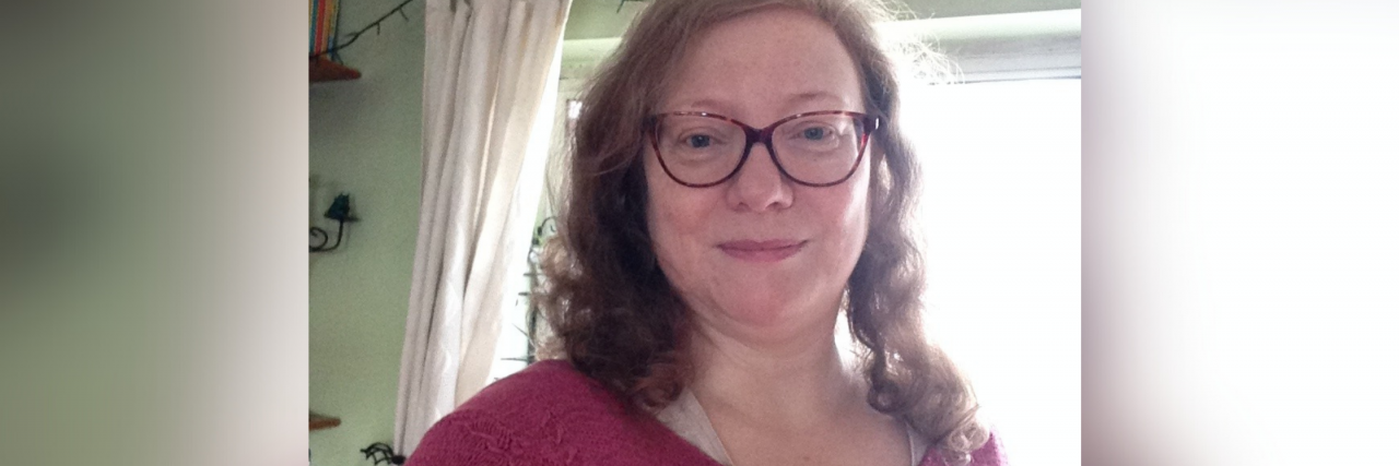 What Helps a Woman in Her Fifties Manage Anxiety A white woman with curly red hair, blue eyes, and glasses, smiles softly at the camera while wearing a red top.