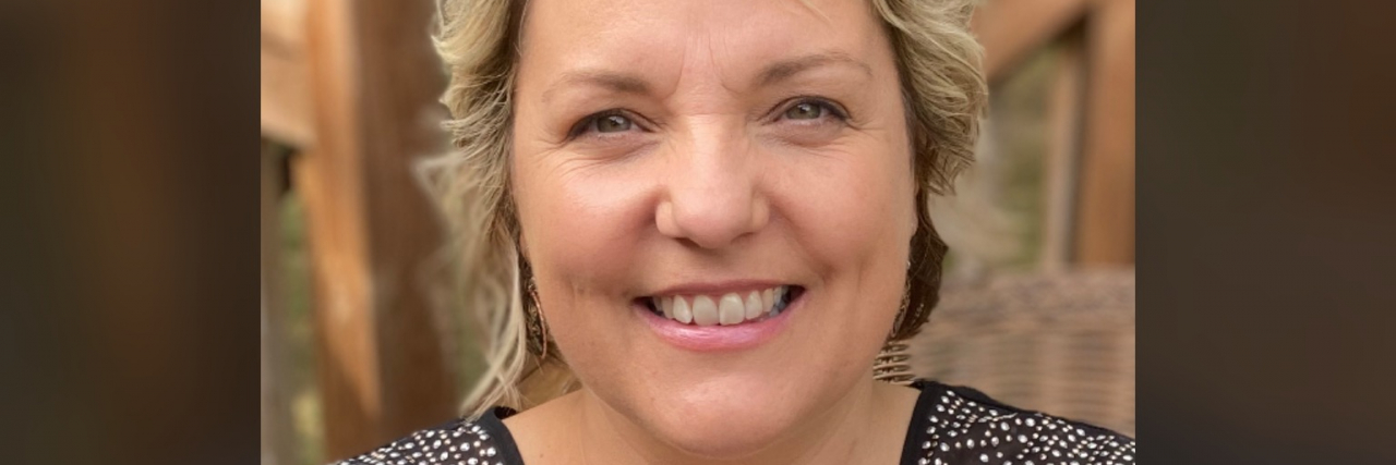 What Helps a Woman in Her Forties With Depression A white woman with short blonde hair wearing a black short-sleeved shirt holds a yellow book.
