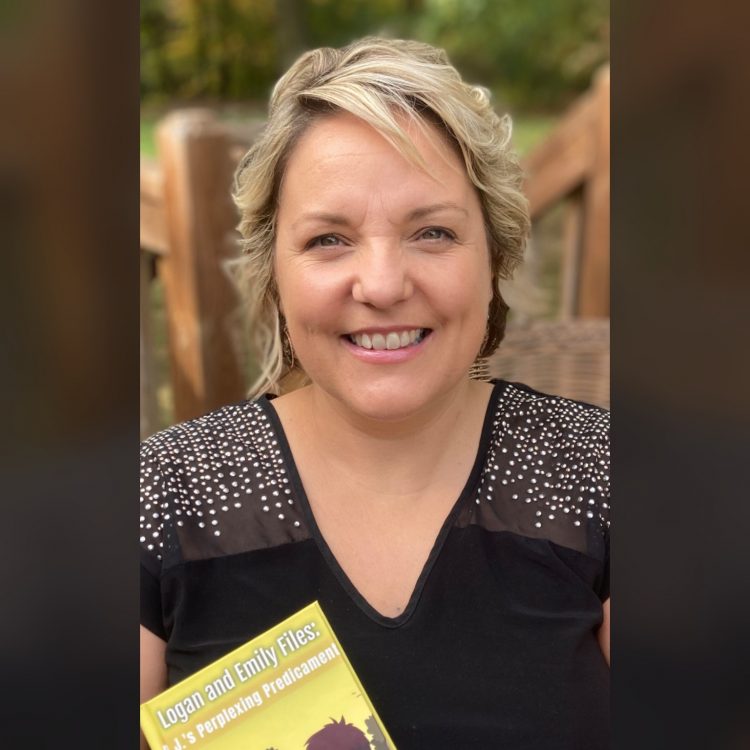 A white woman with short blonde hair wearing a black short-sleeved shirt holds a yellow book.