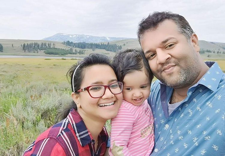 Purnima and her husband stand outside with their daughter between them.