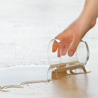 Woman picking up a drinking glass of water spilled on the floor.