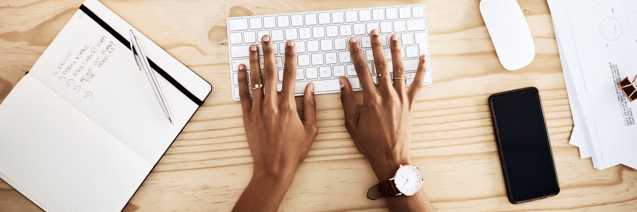 Person working at a desk with to-do list. Close up of hands on keyboard.