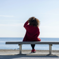 Rear view of a young black woman sitting on a bench while looking away to the horizon over the sea