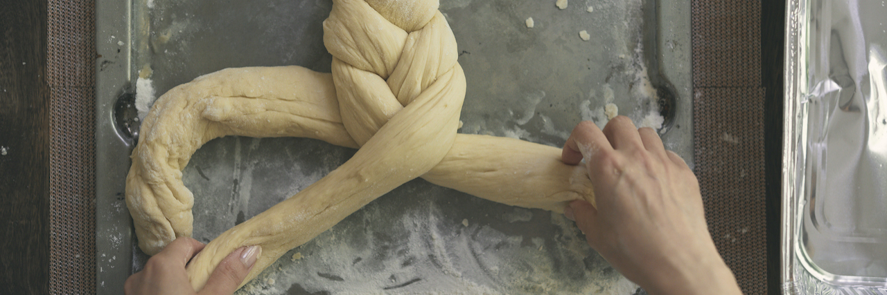 Hands braiding dough for Challah bread on baking sheet