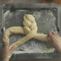 Hands braiding dough for Challah bread on baking sheet