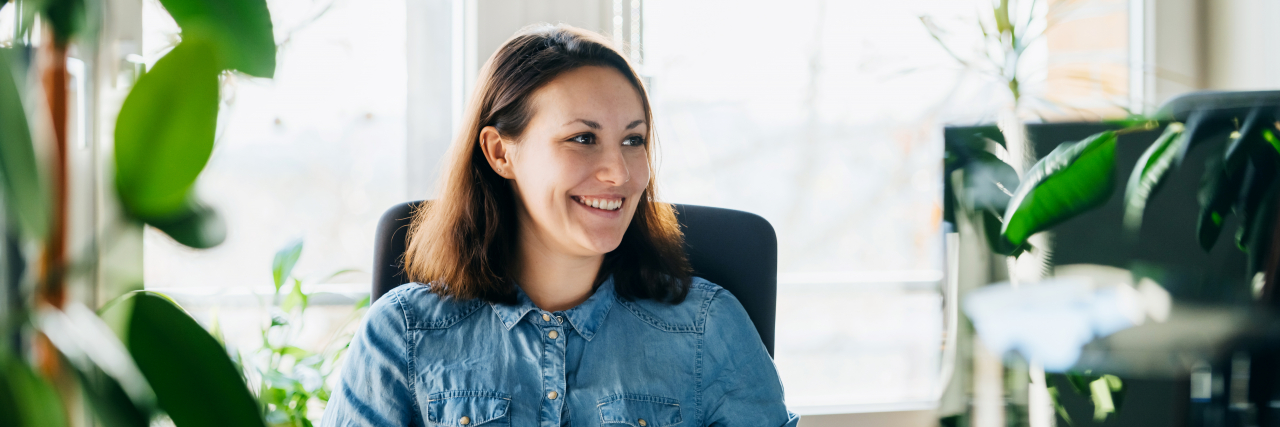 Advocating for Myself in the Workplace With Rheumatoid Arthritis A woman sitting at her computer desk smiling while working.