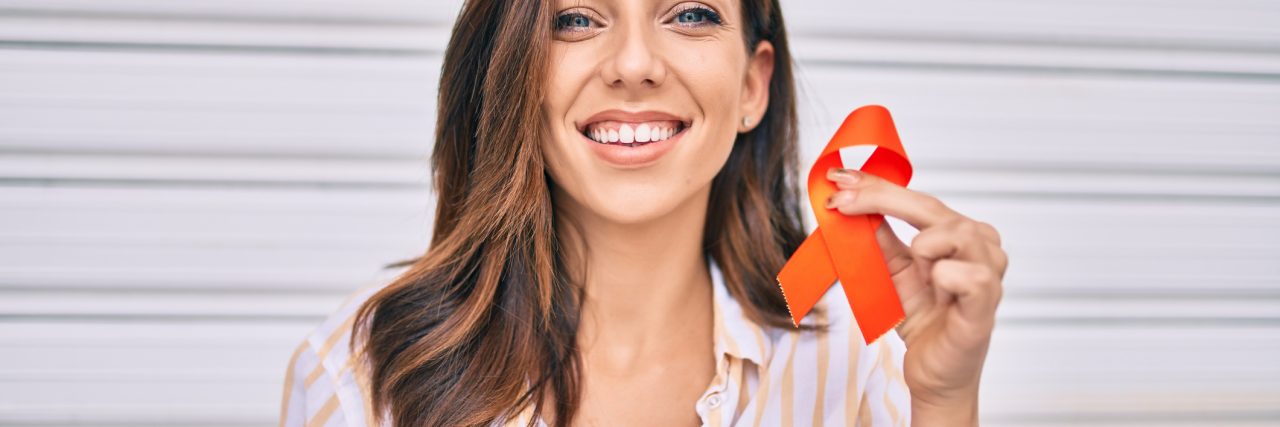 Young hispanic woman smiling happy holding awareness orange ribbon standing at the city.