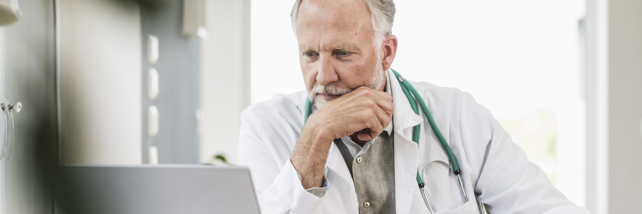 Reddit Thread Shows What Doctors Really Think of Chronic Pain Patients Older white male doctor looking judgmental while using a laptop to talk about chronic pain patients on Reddit.