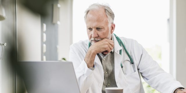 Older white male doctor looking judgmental while using a laptop to talk about chronic pain patients on Reddit.