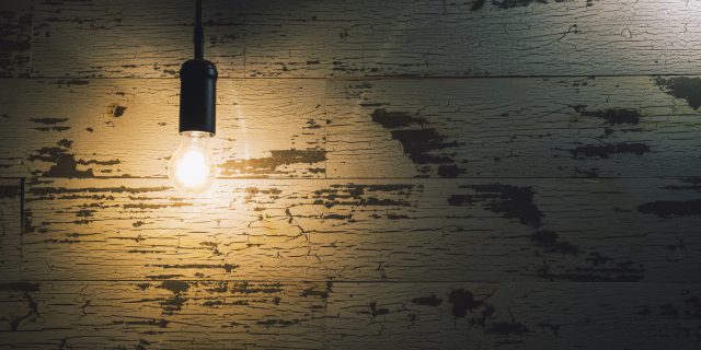 Vintage light bulb hanging against weathered wooden wall in the darkness.