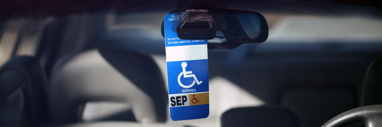 6 Reasons Not to Feel Guilty About Using a Disability Parking Placard Disabled parking permit hanging in the window of a car.