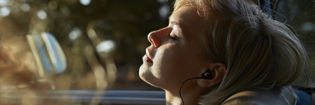 Woman with eyes closed and wearing headphones in car