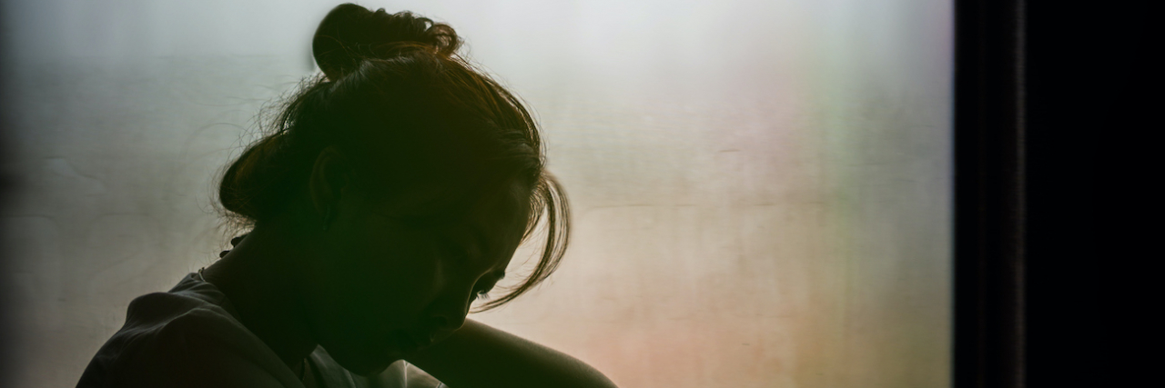 Silhouette of asian woman sitting in window with head facing down
