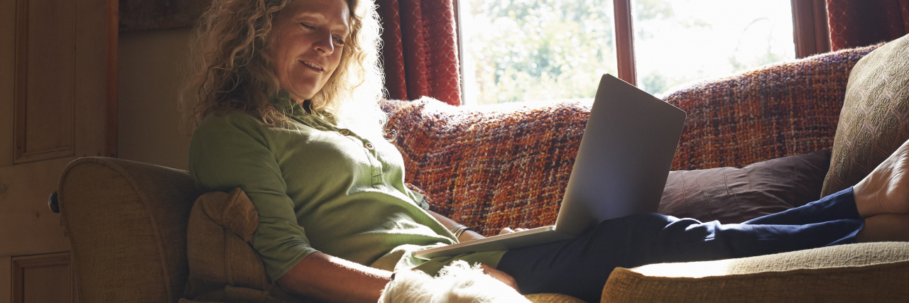 Woman sitting on sofa with laptop and stroking her dog.