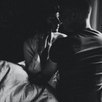 Black and white photo of couple sitting on bed with faces close together