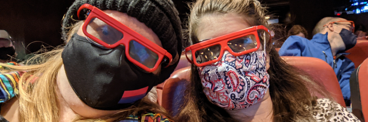 Two women wearing masks and 3D glasses in a theatre.