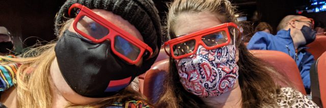 Two women wearing masks and 3D glasses in a theatre.