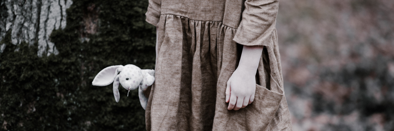 photo of a young girl holding a rabbit plush by her side, wearing a discoloured dress