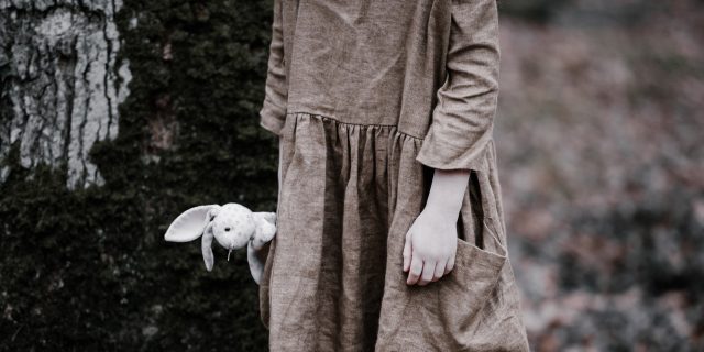 How Old You Were When You Experienced Trauma Matters – Here’s Why photo of a young girl holding a rabbit plush by her side, wearing a discoloured dress