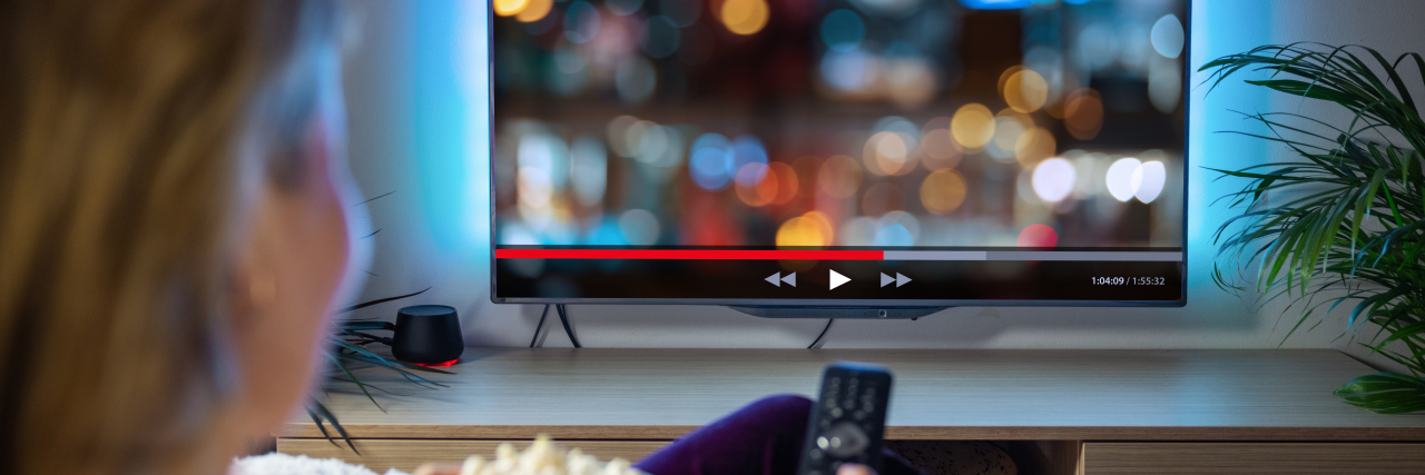 Feeling Like You're the Underdog in a Movie With Chronic Illness A blonde woman wearing purple sweatpants relaxes on the couch with a bowl of popcorn while watching a movie.