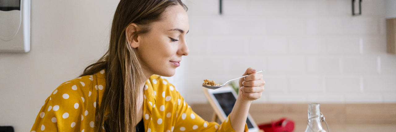 Why Mardi Gras and Ash Wednesday Can Be Hard With an Eating Disorder A woman with long brown hair wearing a mustrad-colored shirt with white polka dots sits at a table while eating breakfast.