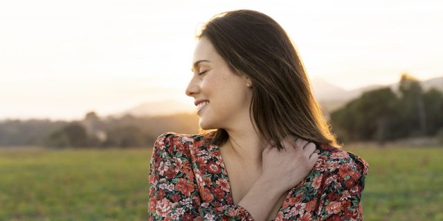 How I'm Finding Self-Worth as a Woman With a Physical Disability A white woman with brown hair wearing a floral blouse hugs herself outside.