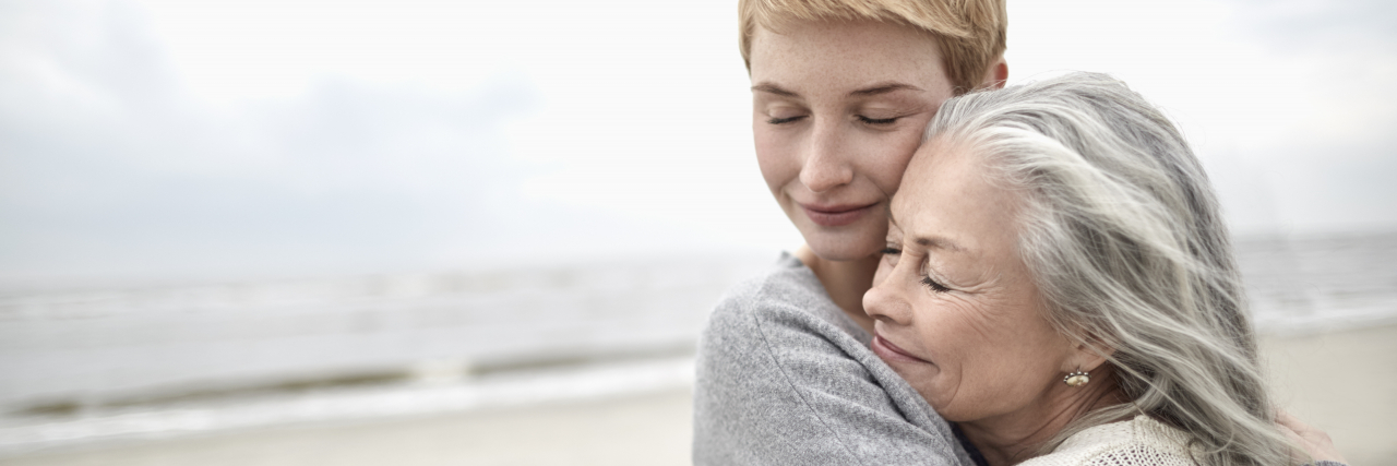Hugging Hurts Me Because of Ehlers-Danlos Syndrome A person with short red hair hugs a woman with silver hair on the beach.