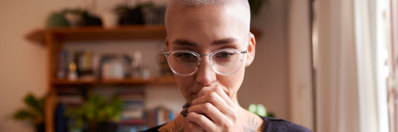 Facing Misdiagnosis and Receiving a Bipolar Disorder Diagnosis A person with short hair and glasses wearing a long-sleeved shirt holds their hands against their mouth while gazing ahead.
