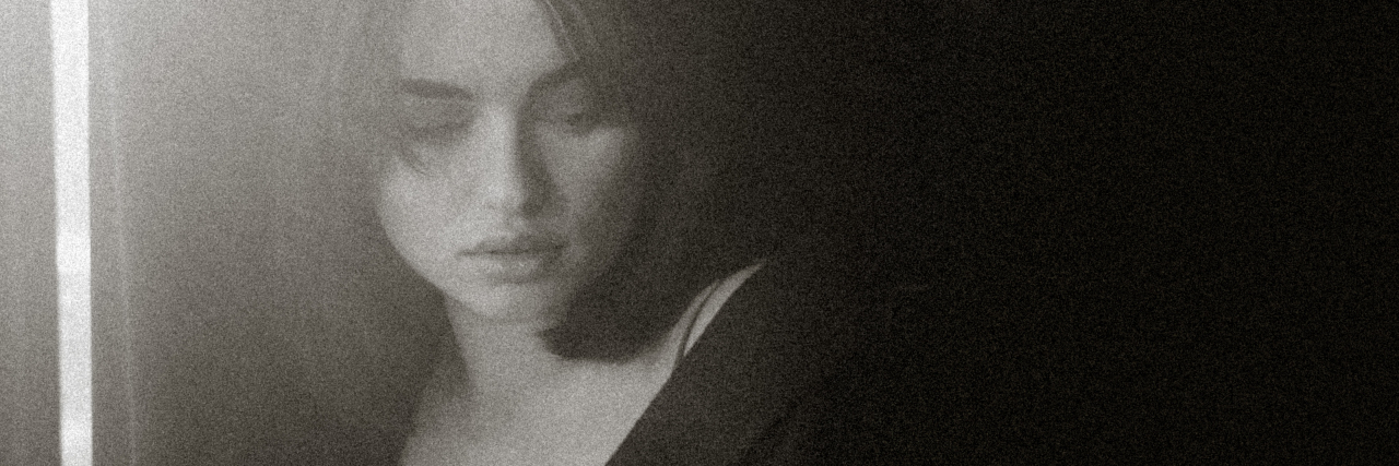 Why Schizophrenia Is a Mortality Risk For COVID-19 black and white photo of a young woman looking back over her shoulder with darkness behind her