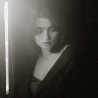 black and white photo of a young woman looking back over her shoulder with darkness behind her