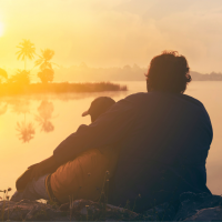 Two people sitting and embracing overlooking water and the sunset