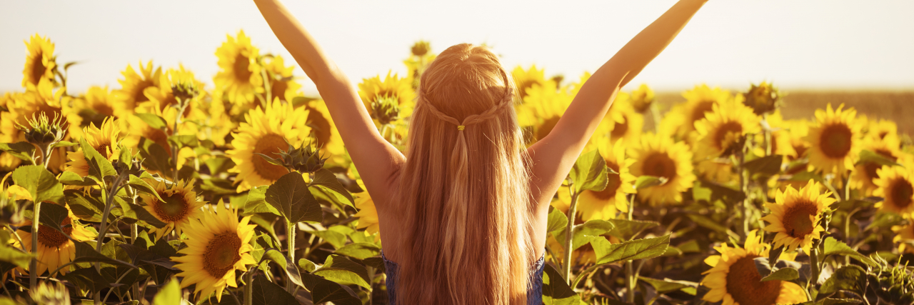 Leaving Your Parent After Years of Their Substance Use A blonde woman wearing a blue dress raises her arms in a field of sunflowers.