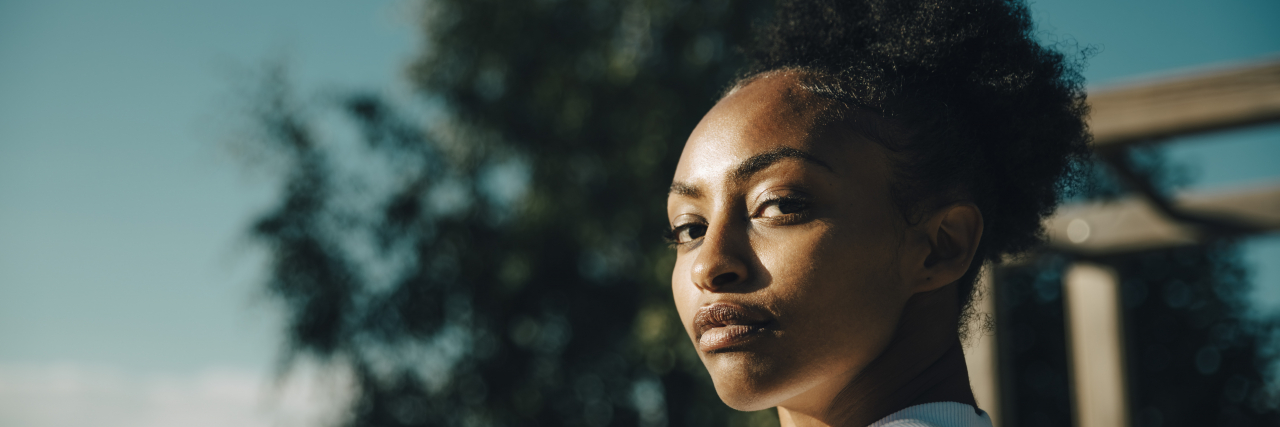 Choosing Not to Have Children as a Woman With Mental Illness A black woman with natural hair pulled back stands outside and looks over her shoulder.