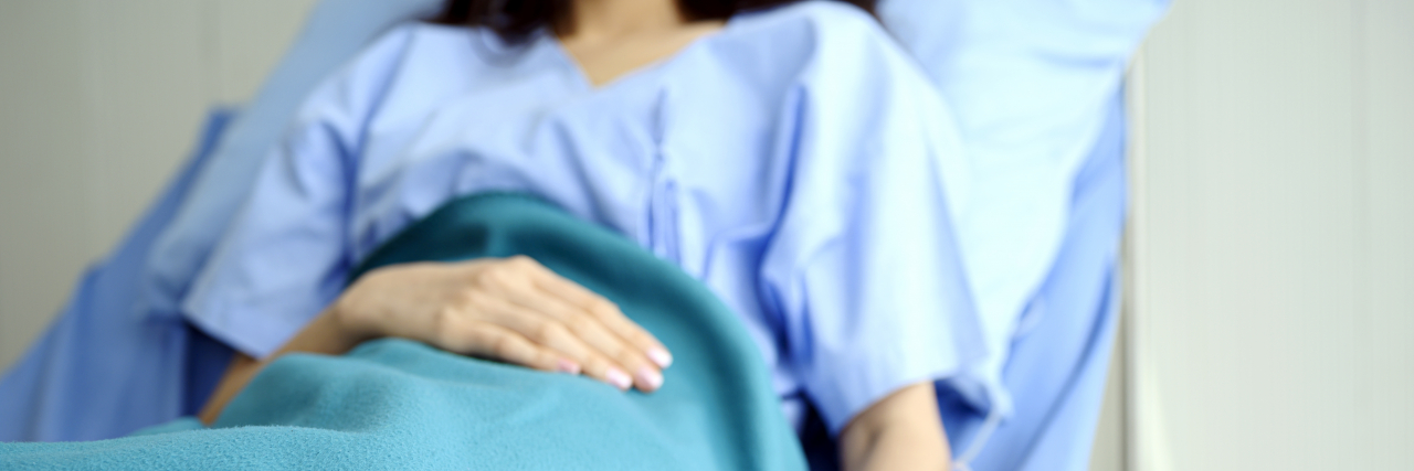 Seeing the Bigger Picture in Stroke Recovery A woman wearing a blue hospital gown lies in a hospital bed with a blue blanket covering her.